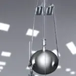 Ein klassisches Labor-Setup mit einem glänzenden Metallpendel, das an einer rostfreien Stahlstange hängt, steht auf einer weißen Arbeitsfläche. Im Hintergrund ein großes, transparentes Messgerät mit einer Skala von 0 bis 10 Newton, das die Kraftme…