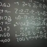 Mathematiker schreibt Primzahlen an Tafel, während digitale Überlagerung großer Primzahlen und modularer Gleichungen leuchtet; feiner Kreidestaub betont die präzisen Striche.