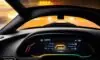 Nahaufnahme eines Armaturenbretts eines Elektroautos bei Nacht, auf dem eine gelbe Warnleuchte auf dem Display leuchtet und eine dramatische Atmosphäre erzeugt.