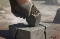 Nahaufnahme eines rostigen Eisenbrechstabs, der einen schweren Steinblock aus dem Boden hebelt, um das Hebelprinzip zu veranschaulichen.